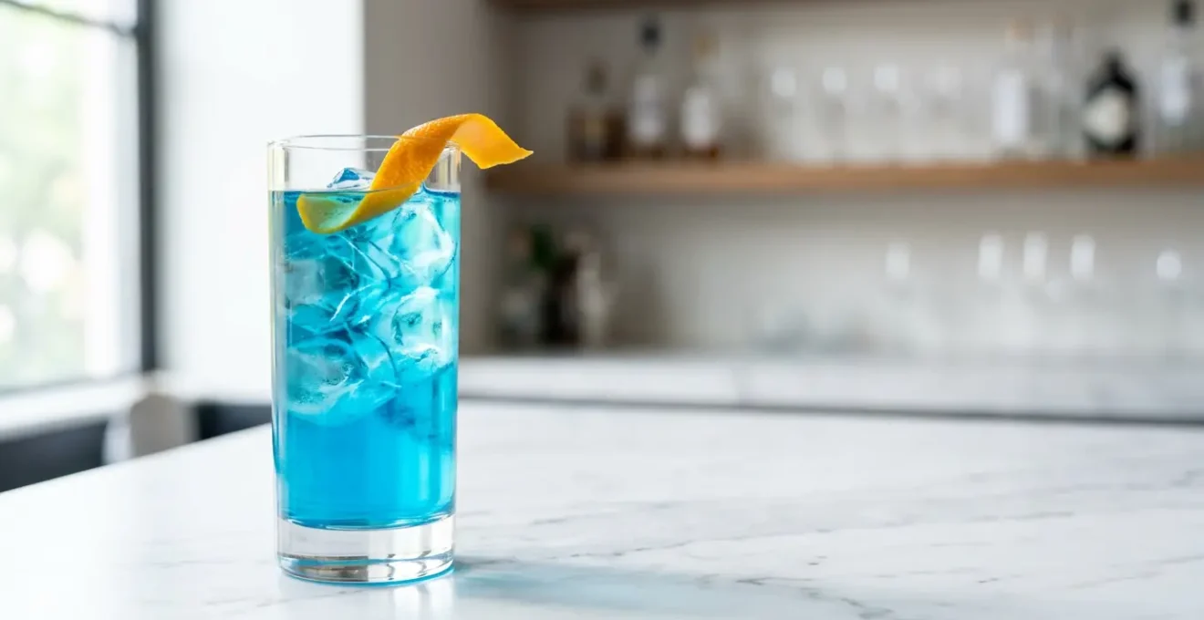 Cocktail Blue Lagoon au bleu électrique intense dans un verre highball minimaliste avec glaçons transparents et zeste d'orange