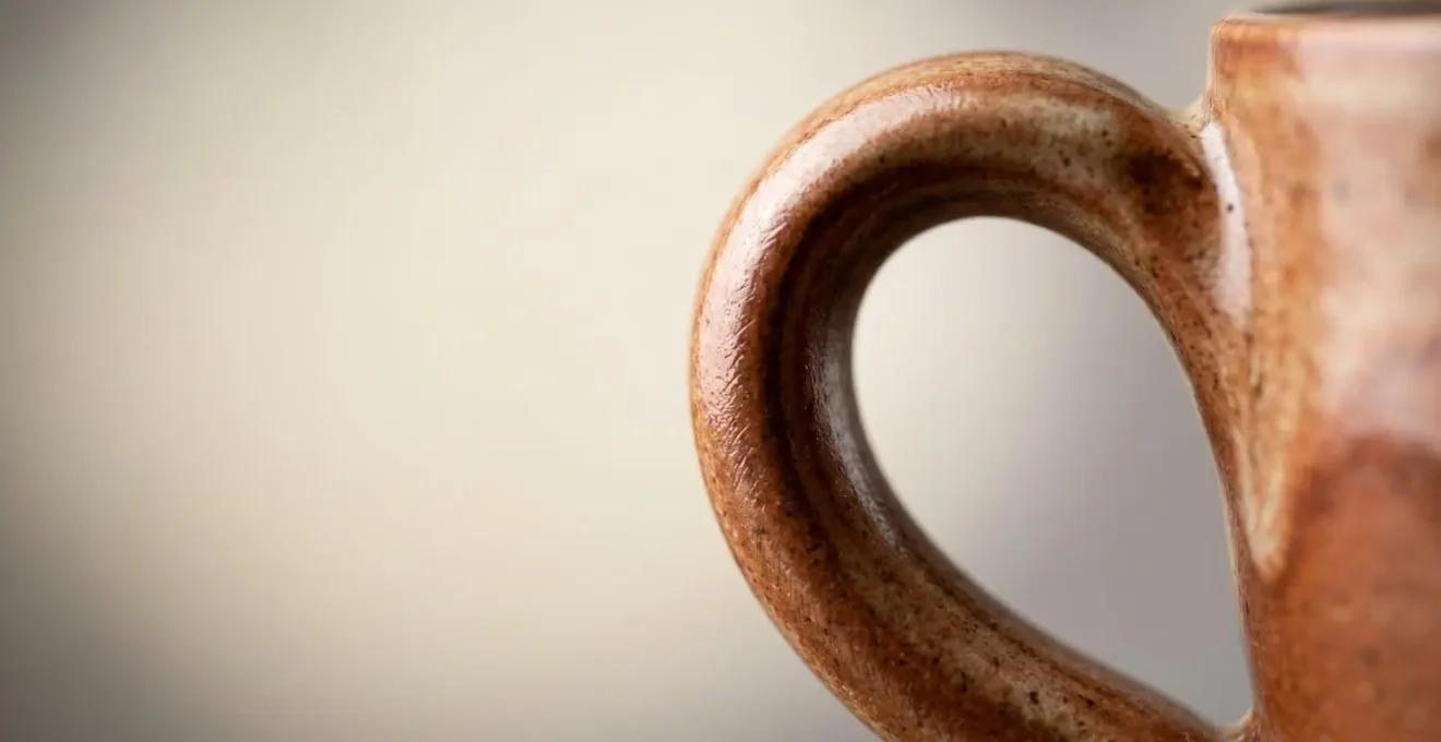 Vue macro détaillée de l'anse d'une tasse en céramique artisanale montrant la texture et la forme ergonomique