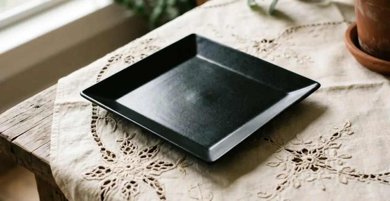 Contraste élégant entre une assiette contemporaine géométrique posée sur un linge ancien brodé de motifs floraux délicats