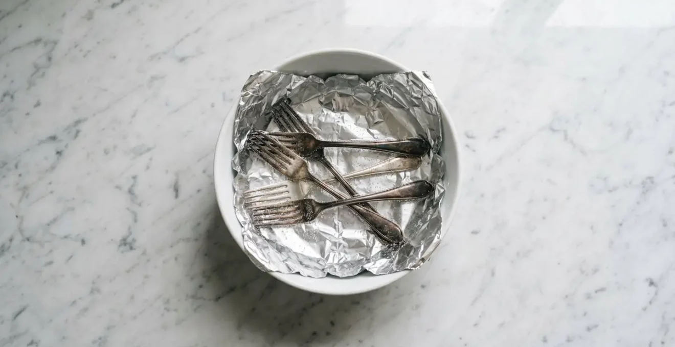 Vue en plongee d une bassine avec papier aluminium et couverts en argent dans eau chaude