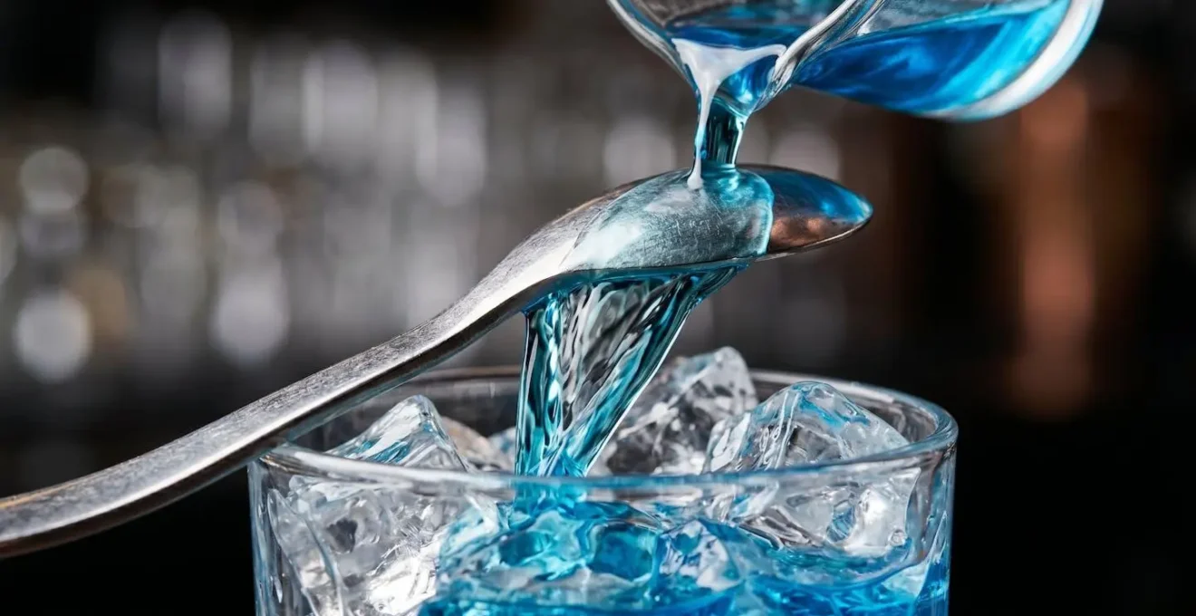 Gros plan sur la technique de la cuillère de bar versant du liquide bleu créant un effet de stratification dans un verre avec glace