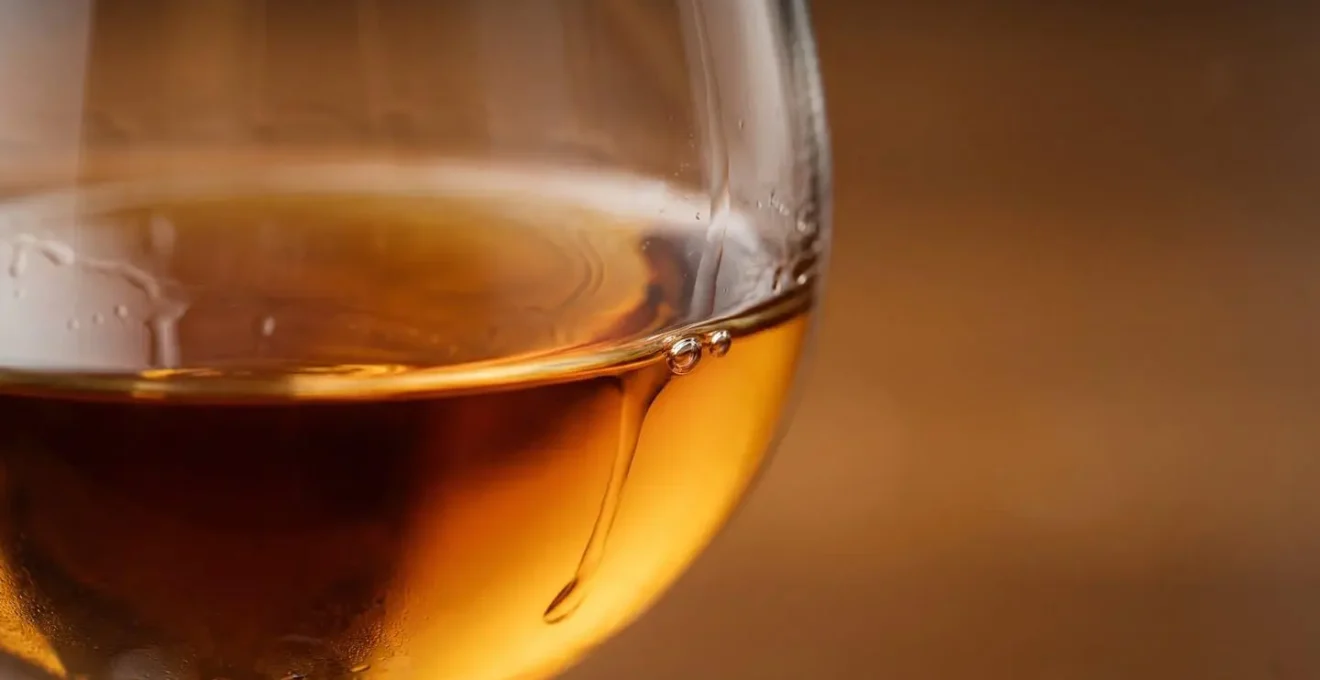 Gros plan d'un verre tulipe rempli de cognac ambré sur une surface réfléchissante avec un éclairage latéral doux